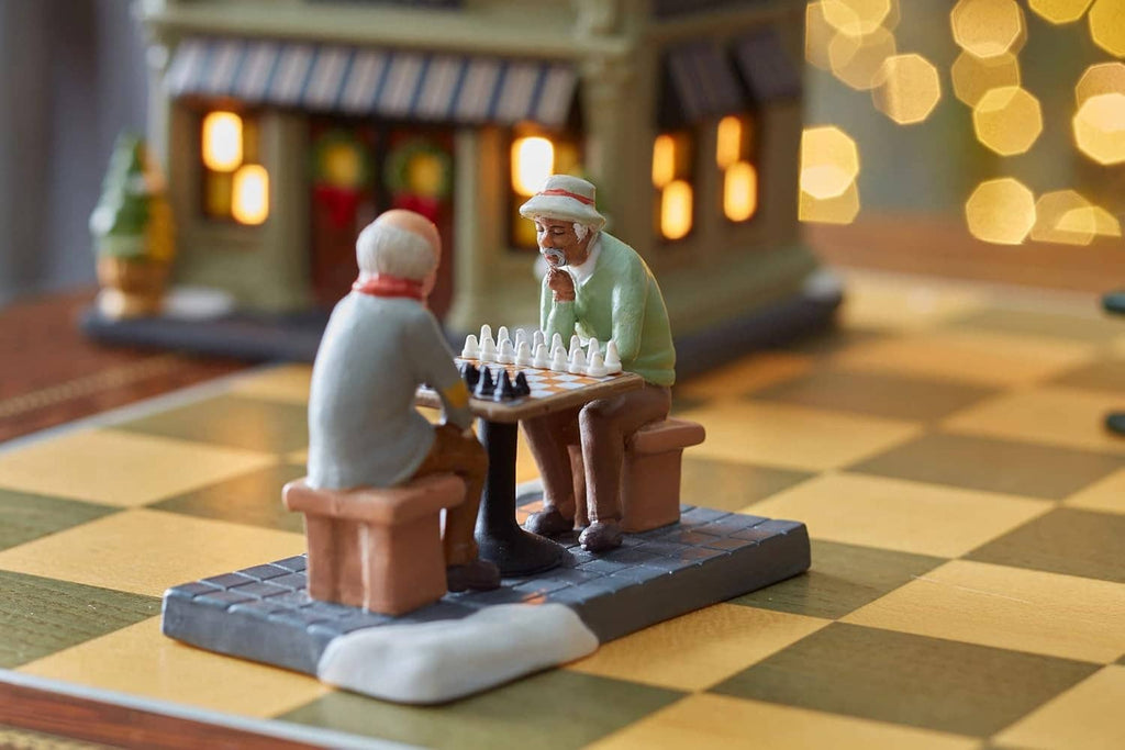 Mini chess figurine set with two seated men facing each other over an orange-brown chessboard.