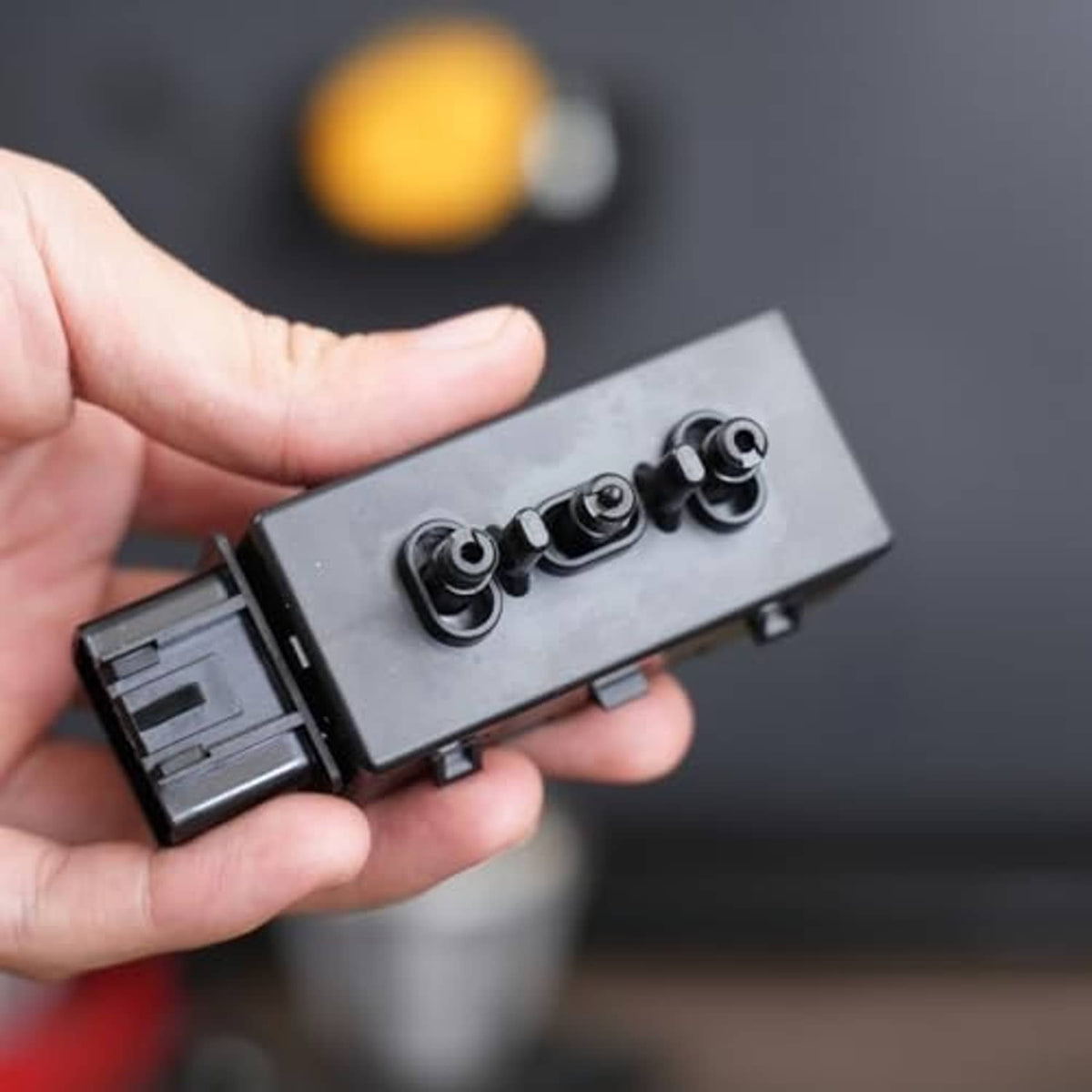 Power seat switch connector held in hand, showing top pin ports and gray housing