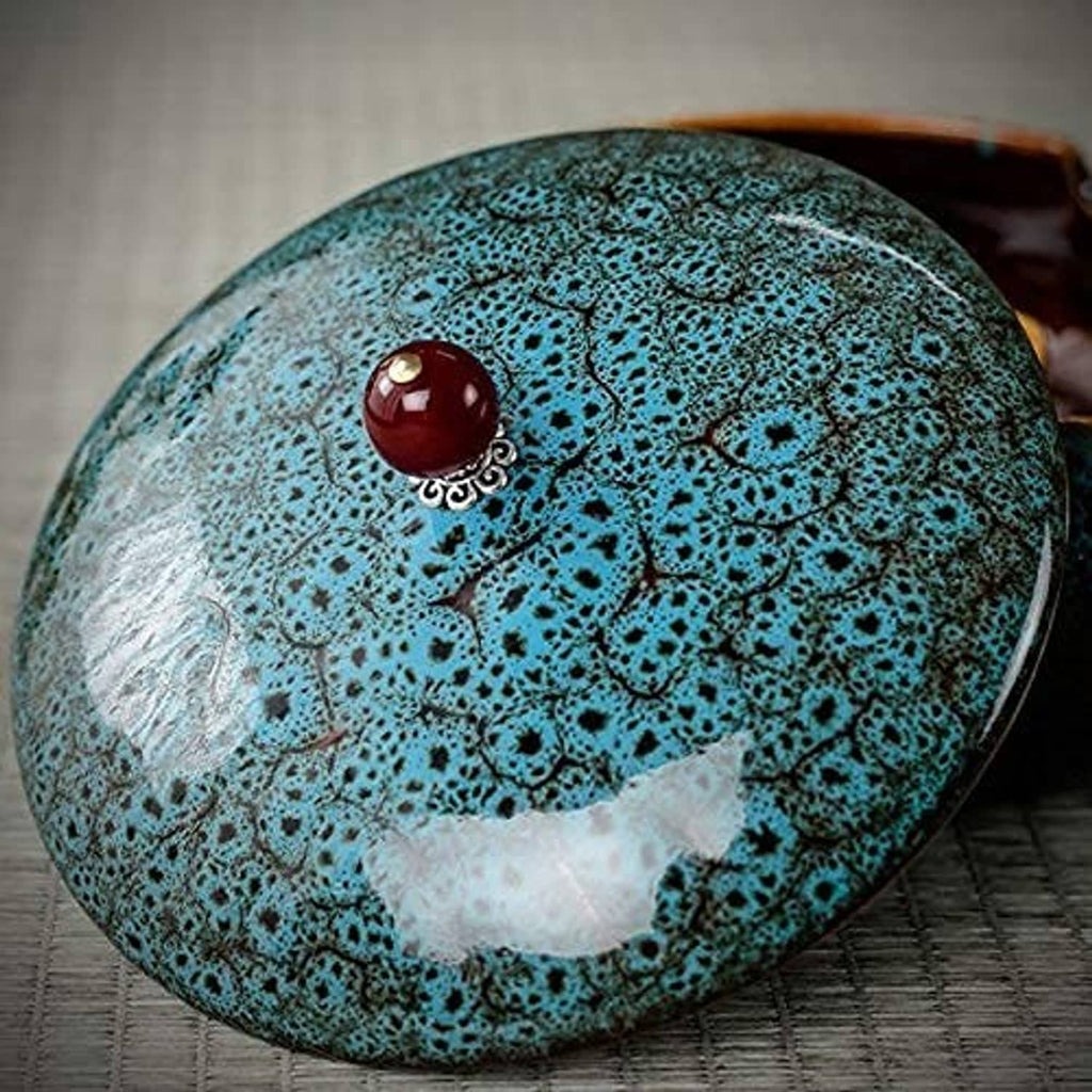 Turquoise ceramic ashtray lid with ornate red knob, close-up on tabletop