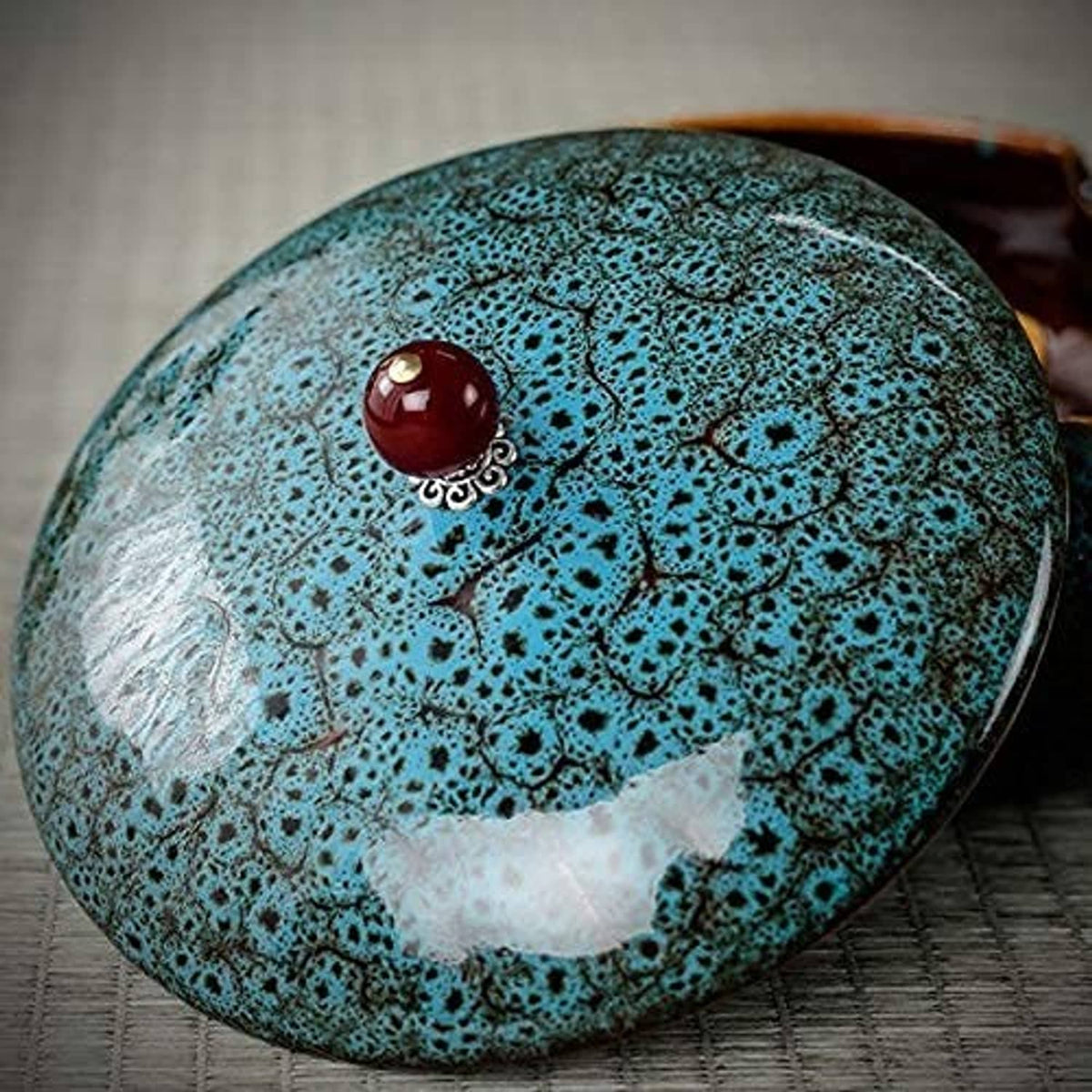 Turquoise ceramic ashtray lid with ornate red knob, close-up on tabletop