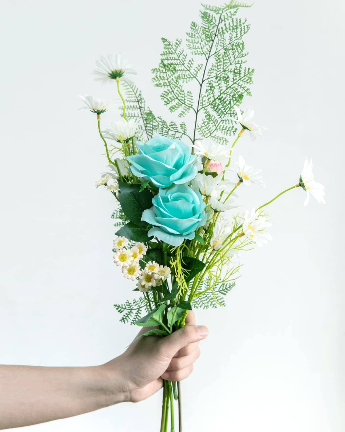 Handheld bouquet of teal blue artificial roses with white blossoms and fern greenery