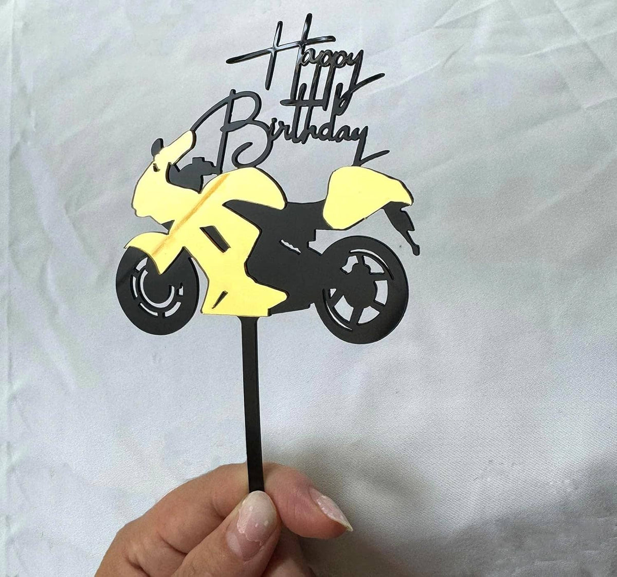 Hand holding a motorcycle cake topper with black-and-yellow scooter and 'Happy Birthday'