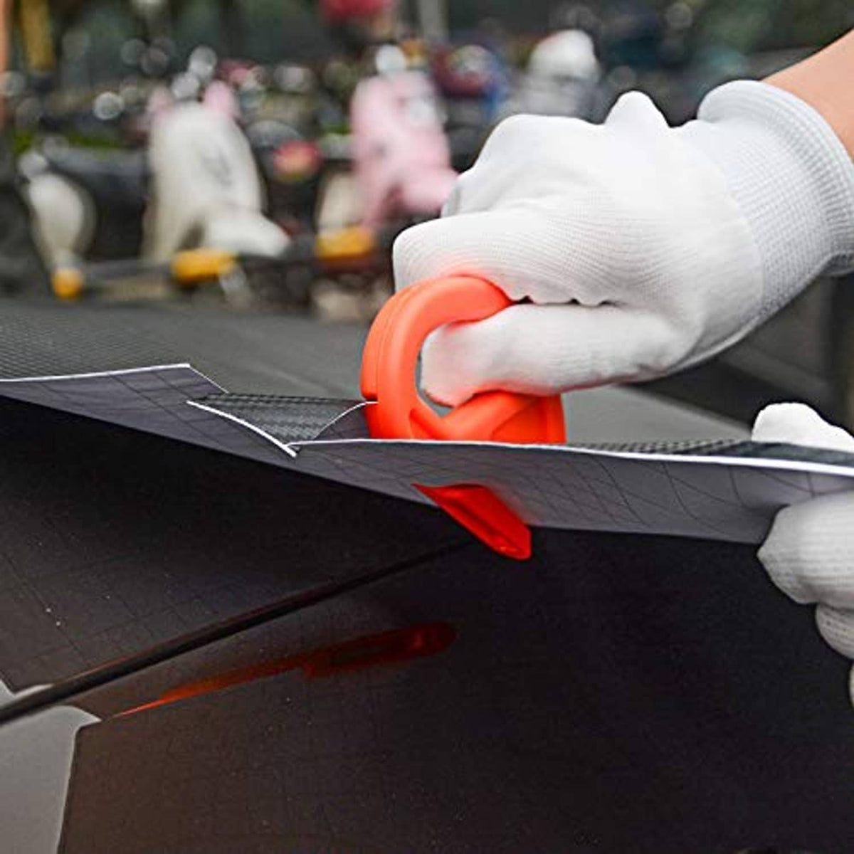 Vehicle vinyl wrap tool kit with orange squeegee being used to smooth dark film