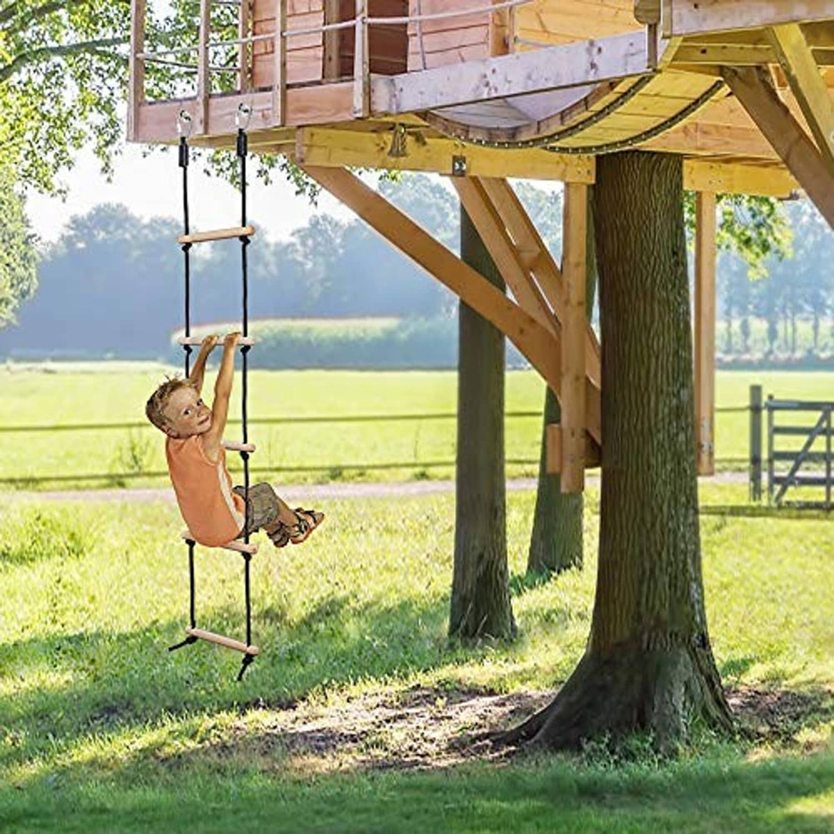 Outdoor rope ladder swing with wooden rungs, black ropes, hanging from wooden playset
