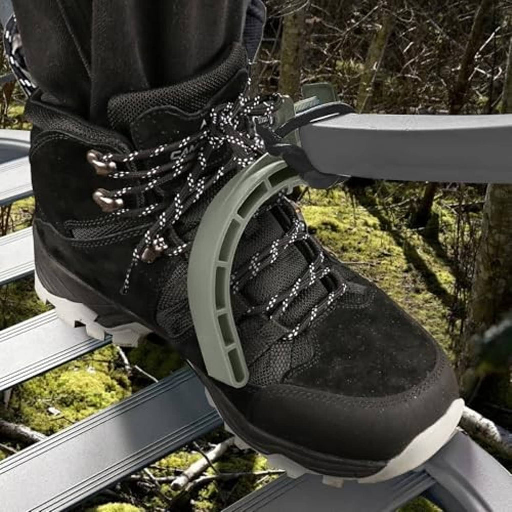 Black laced boot secured in gray climbing stirrup on tree stand rail
