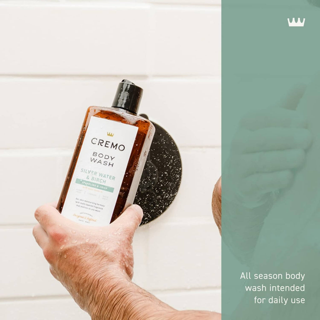 Cremo body wash bottle held in hand with water droplets, black cap and front label