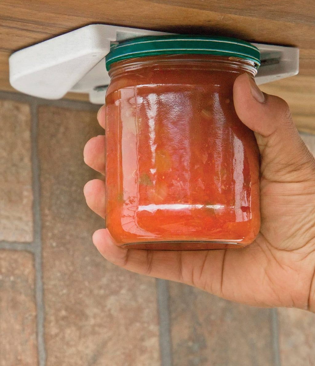 Fox Run under-counter jar opener lifting lid; hand holds glass jar with green top
