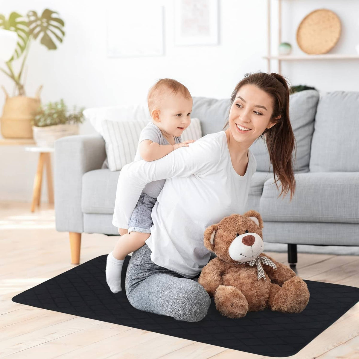 Black washable underpad on the floor with parent and baby seated nearby
