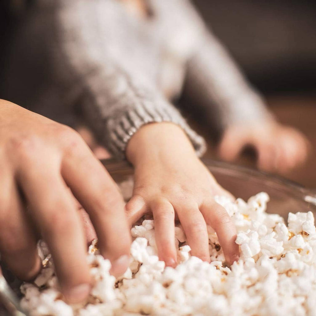 Hands scooping light popcorn kernels from a pile for popping