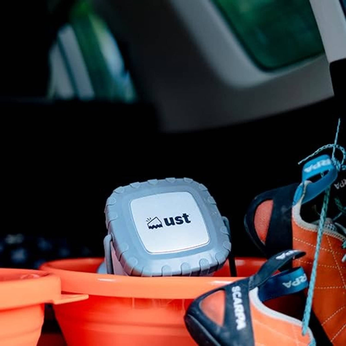 Small gray-white lantern resting on orange outdoor gear beside shoes