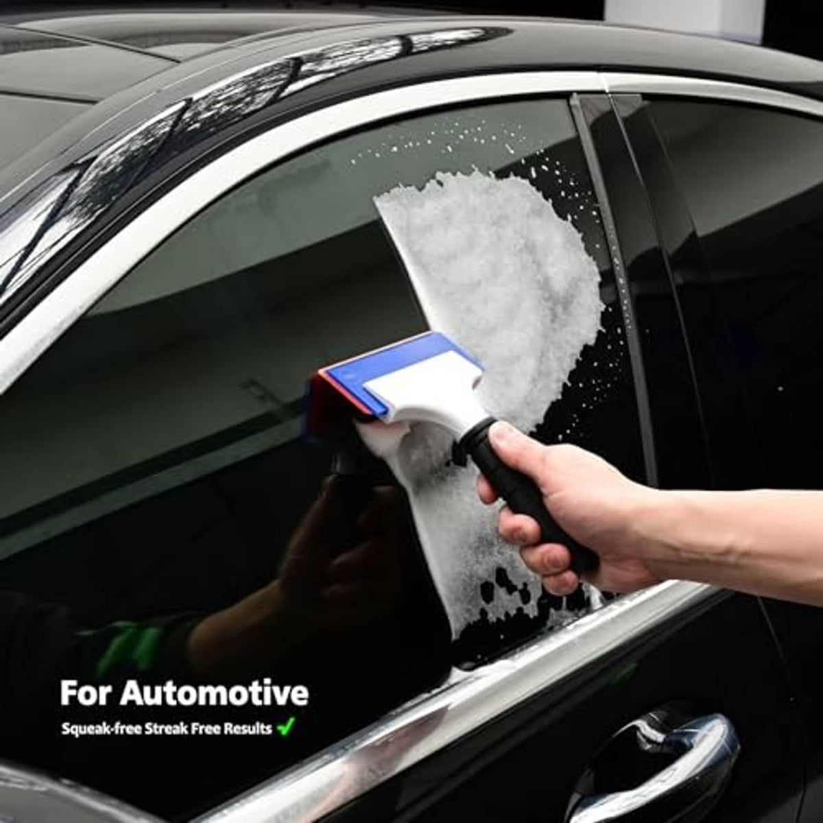 Double-edge squeegee clearing frothy residue from car window, white blade and blue edge.