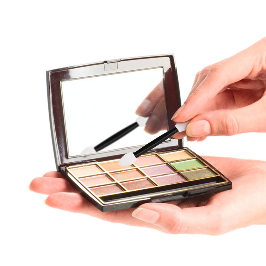 Hand holding makeup palette while using a dual-tip sponge applicator brush with black handle