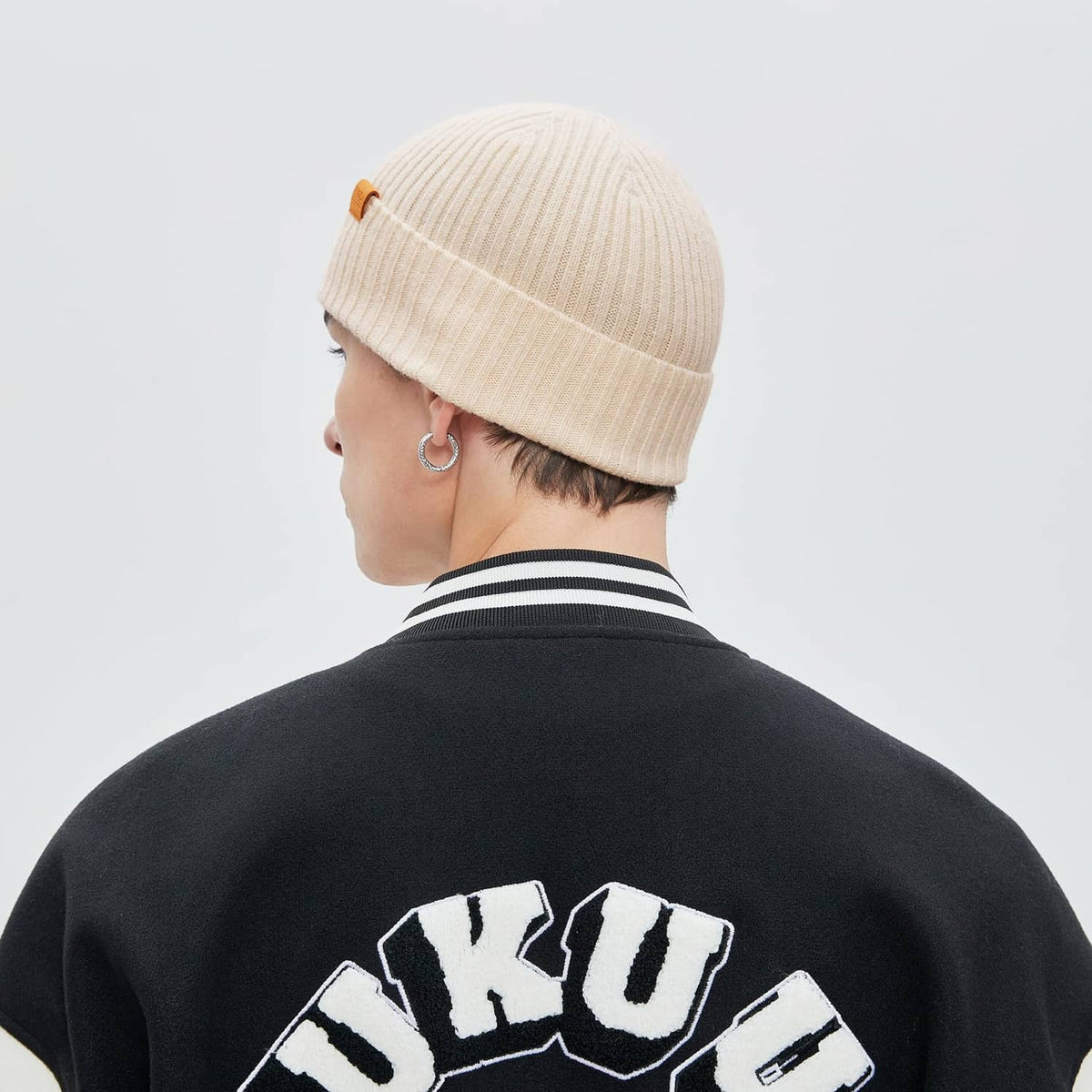 Beige knit beanie worn backward with folded cuff and ribbed texture
