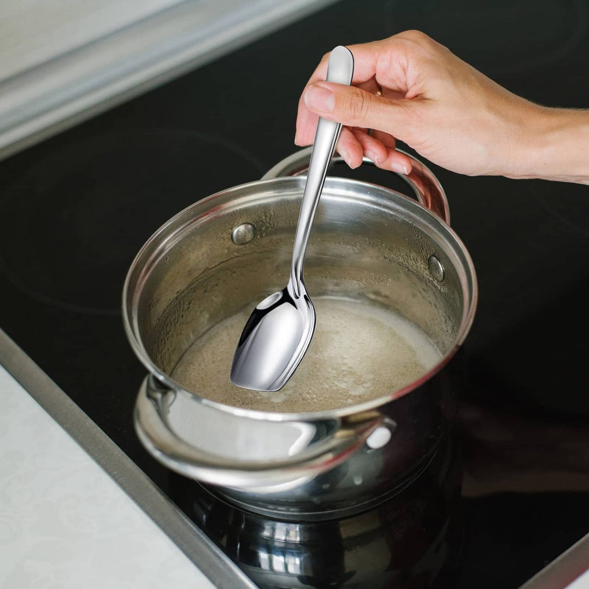 Silver serving spoon with oval bowl and flat bottom, held over saucepan