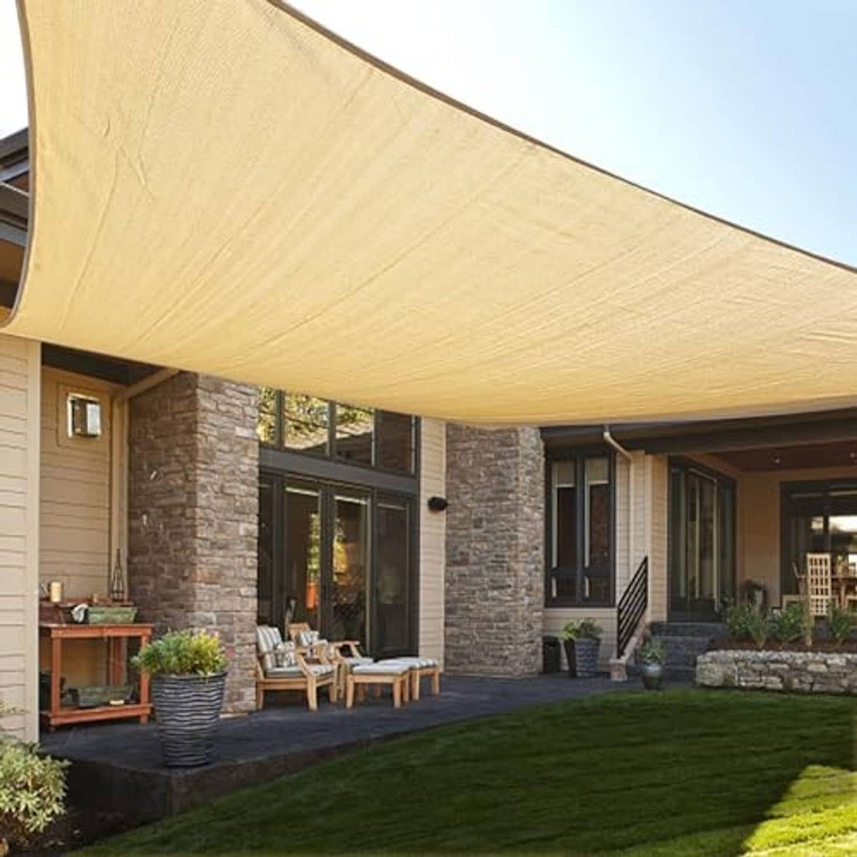 Tan rectangle sun shade sail canopy over backyard patio next to green lawn