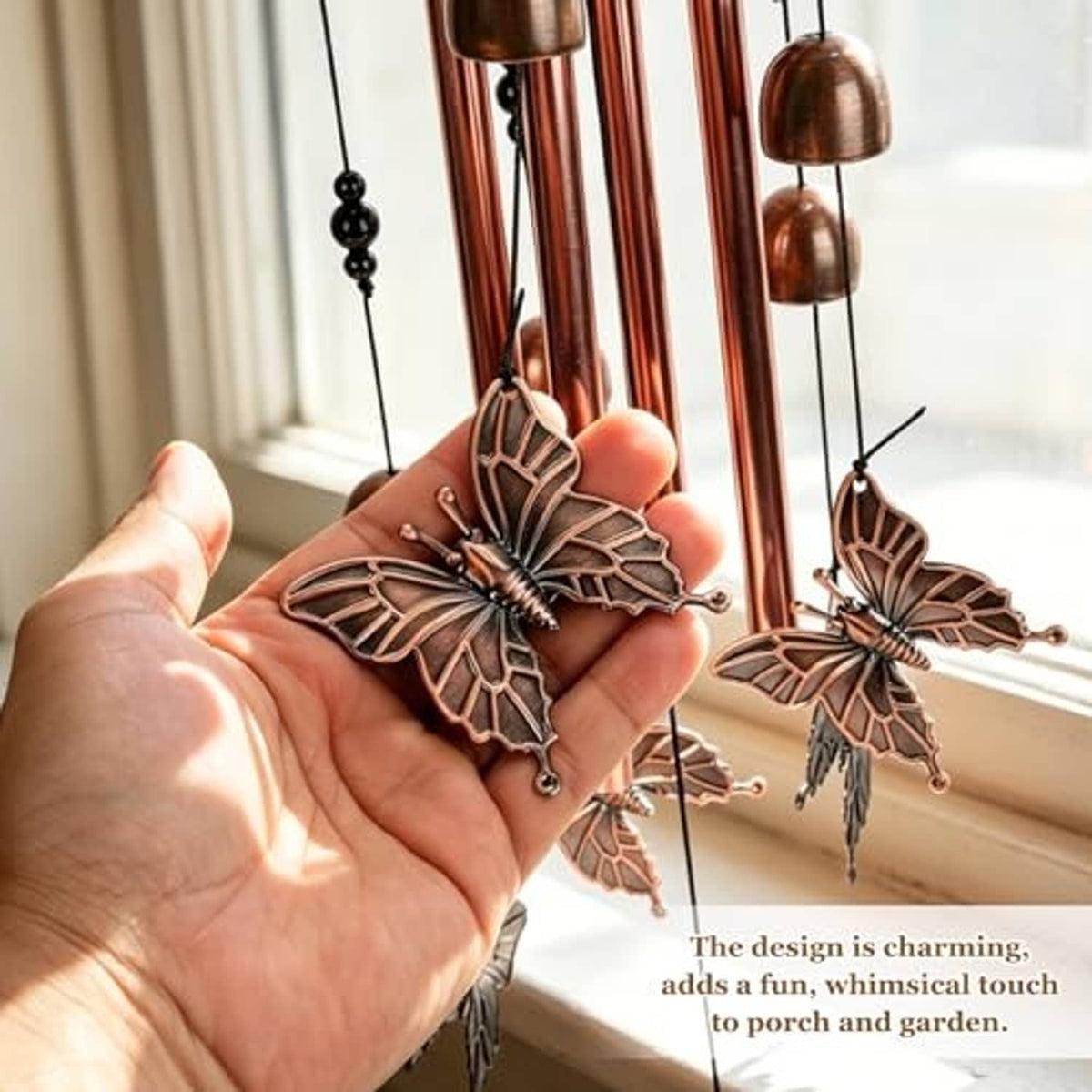 Copper-tone butterfly wind chime charms on hanging rods, held in a hand