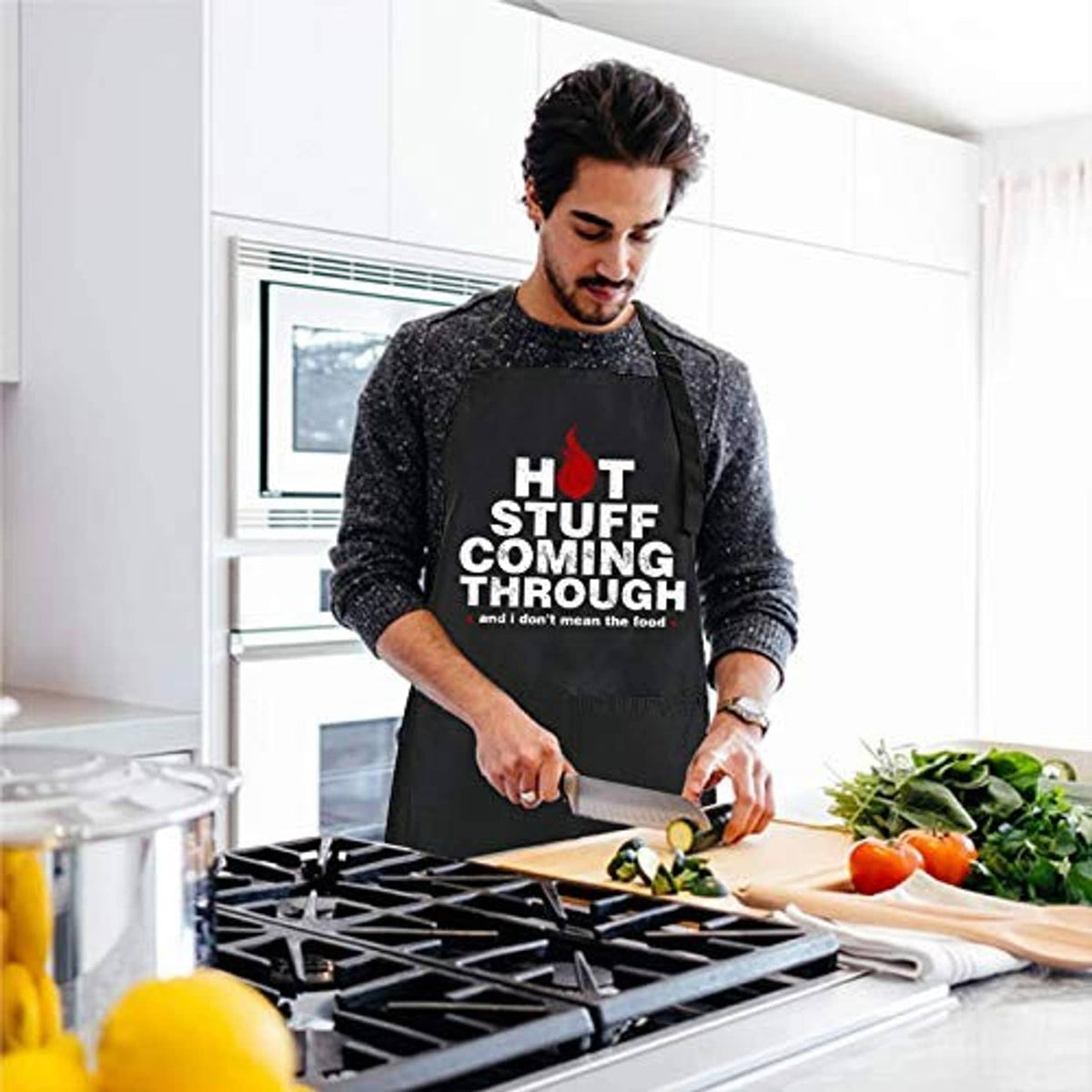 Man wearing black chef apron with “HOT STUFF COMING THROUGH” slogan in the kitchen