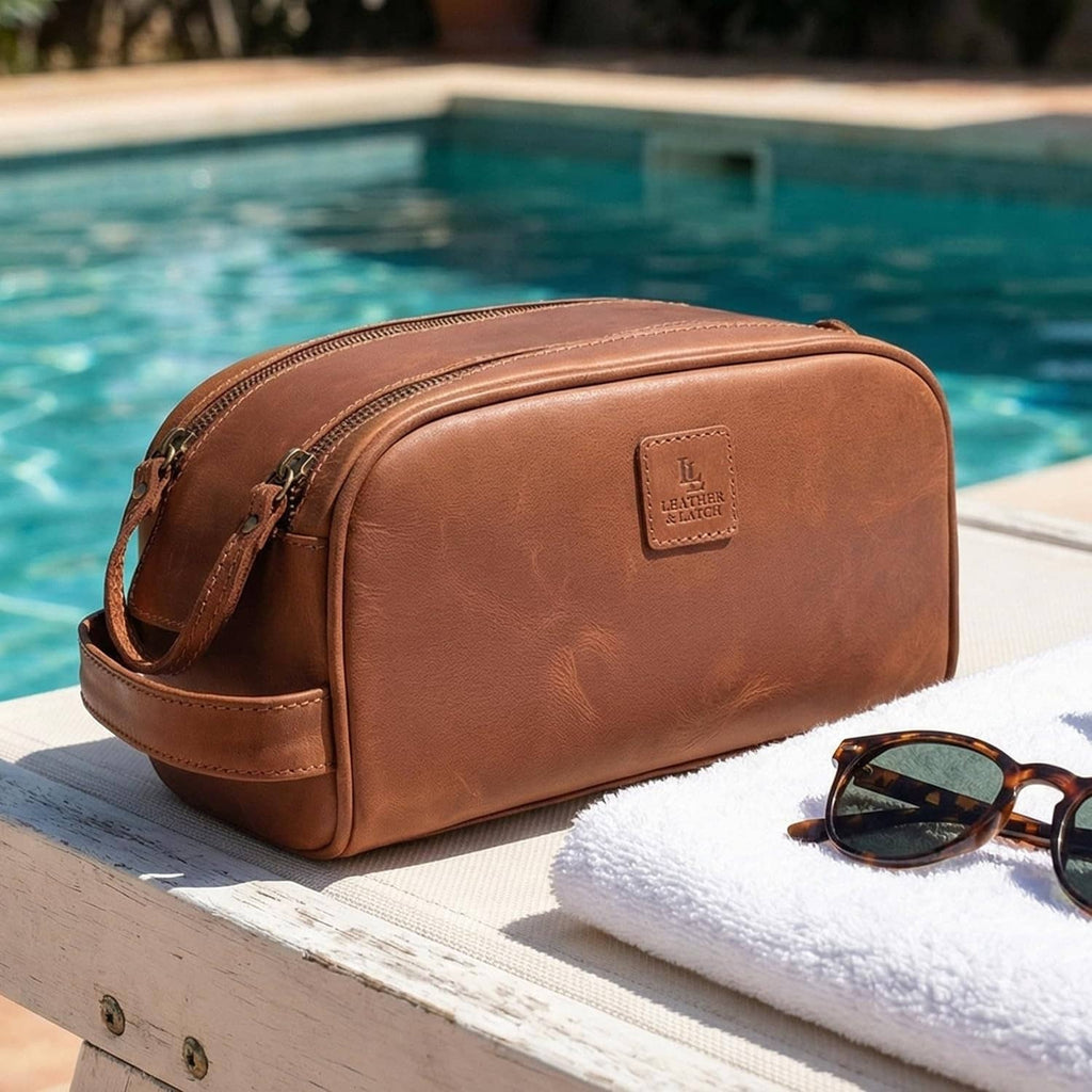 Brown leather toiletry bag with front logo patch and side carry strap