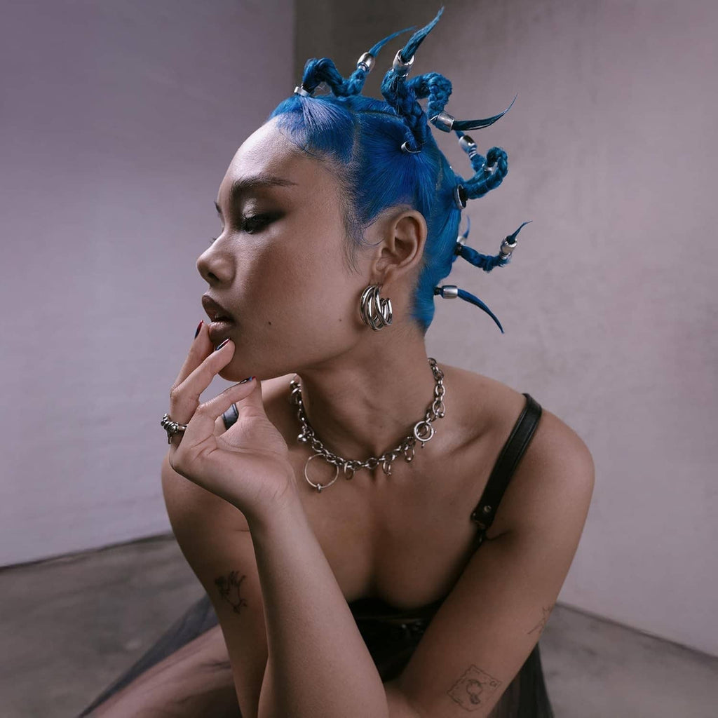 Side profile of woman with bright blue braided spiky hair and hoop earrings
