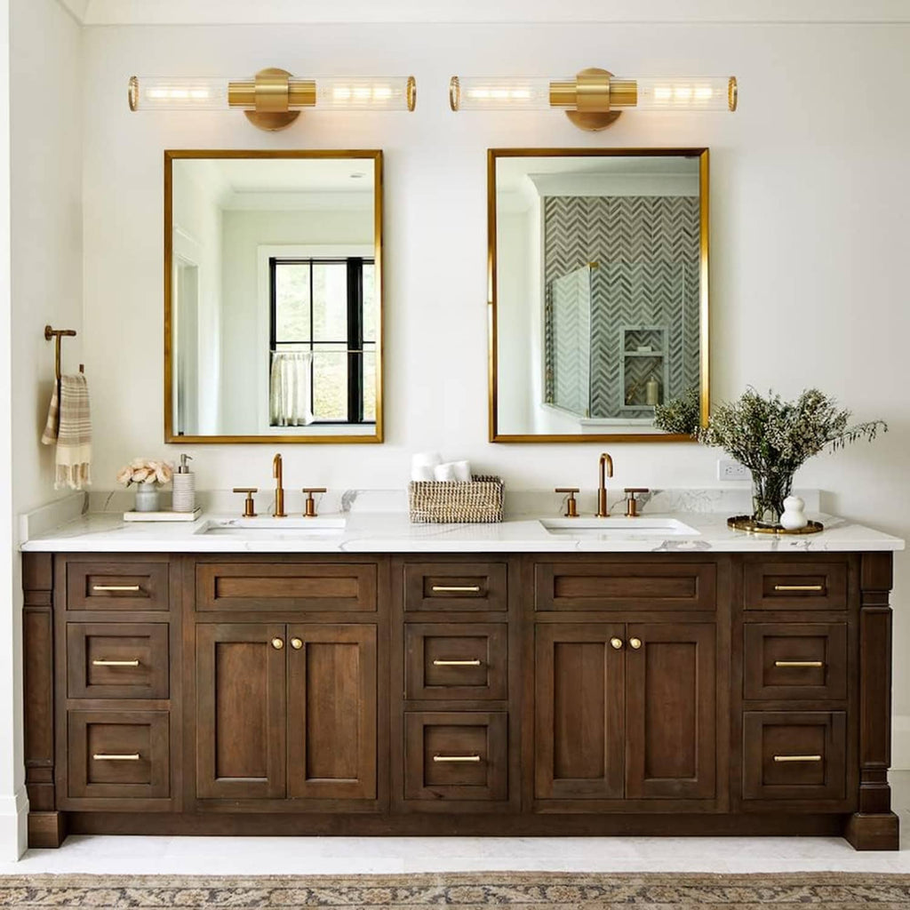Gold vanity light 2-pack with clear glass tube shades mounted on wall over mirrors.
