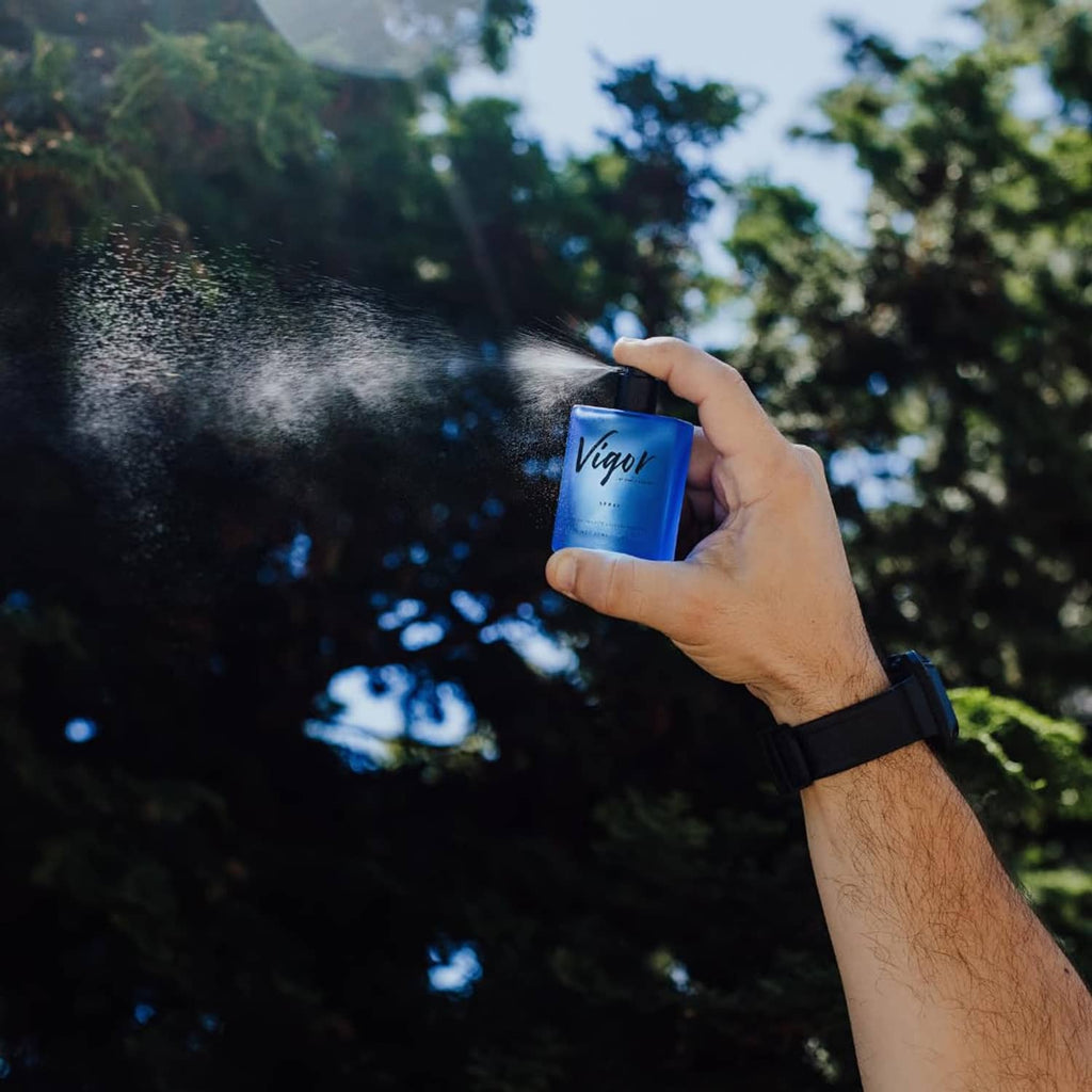 Vigor cologne bottle being sprayed outdoors, blue mist near the nozzle