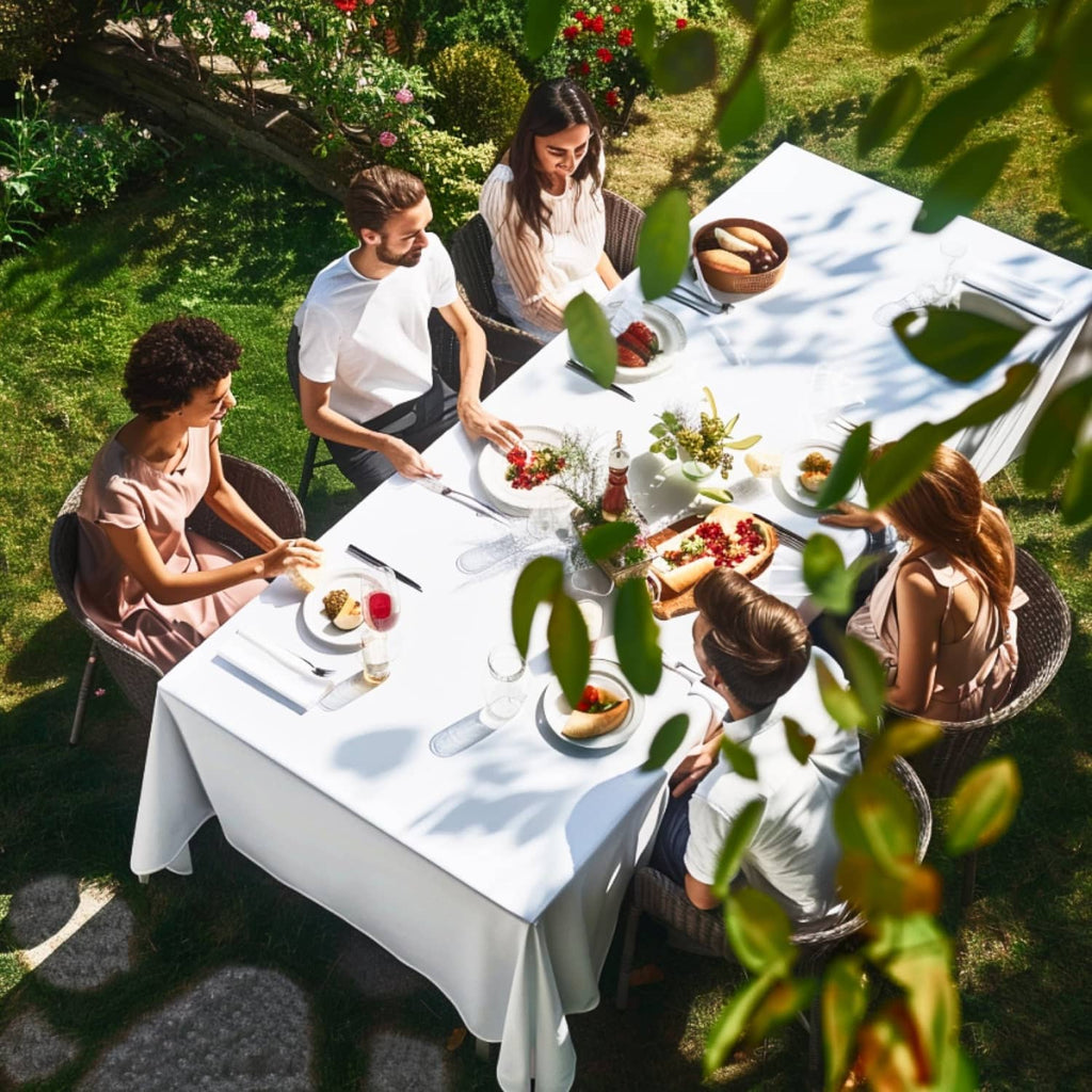White tablecloth on outdoor dining table with people eating in a garden