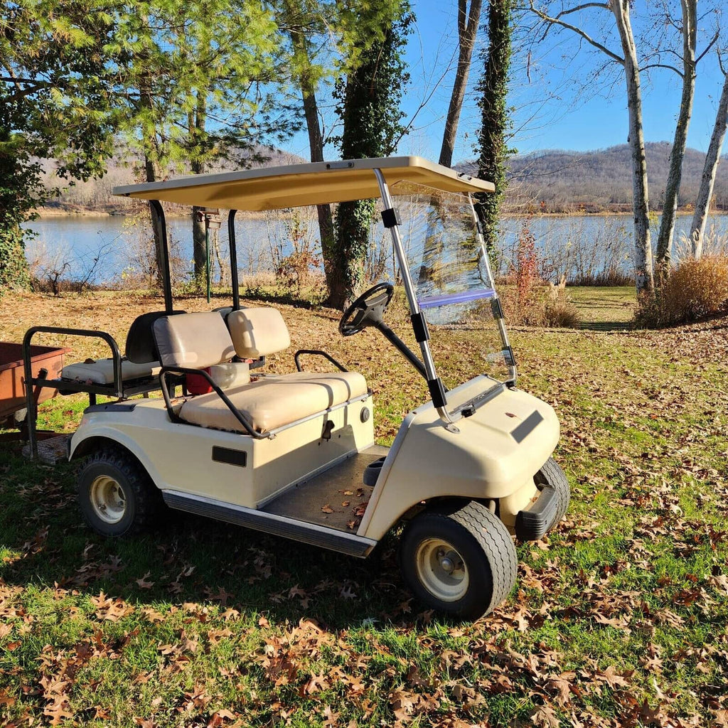 Clear folding windshield with black frame on a beige golf cart, three-quarter view