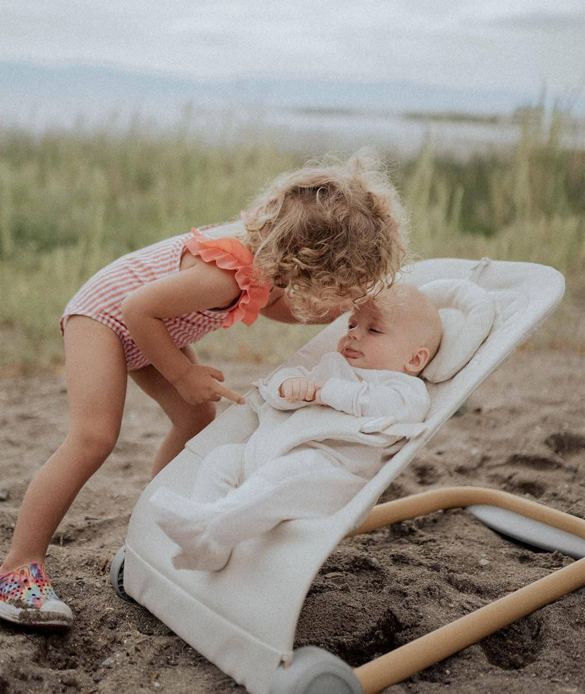 Portable baby bouncer on outdoor ground with infant reclining and harness secured