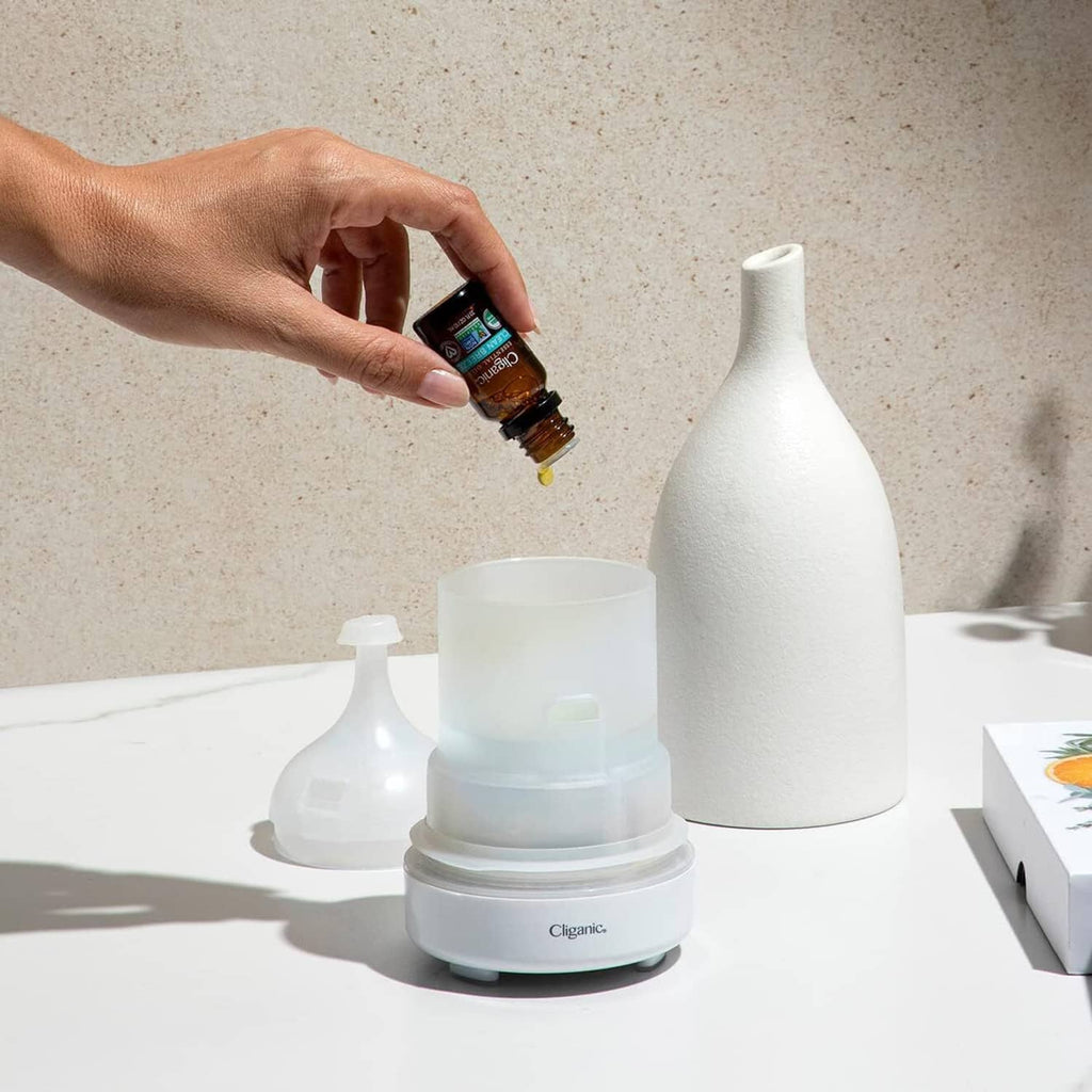 Lavender essential oil bottle being applied with hand near white aroma diffuser.