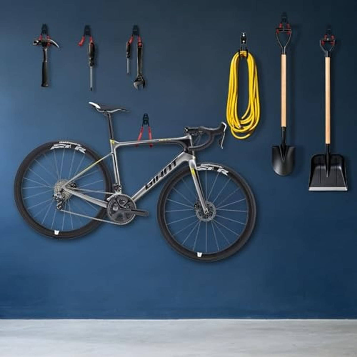 Wall-mounted orange wave hooks holding a bicycle, shovel, and gardening tools