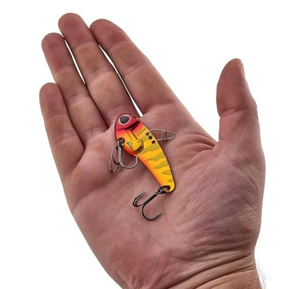 Blade bait fishing lure held in hand; yellow-red body with treble hooks.