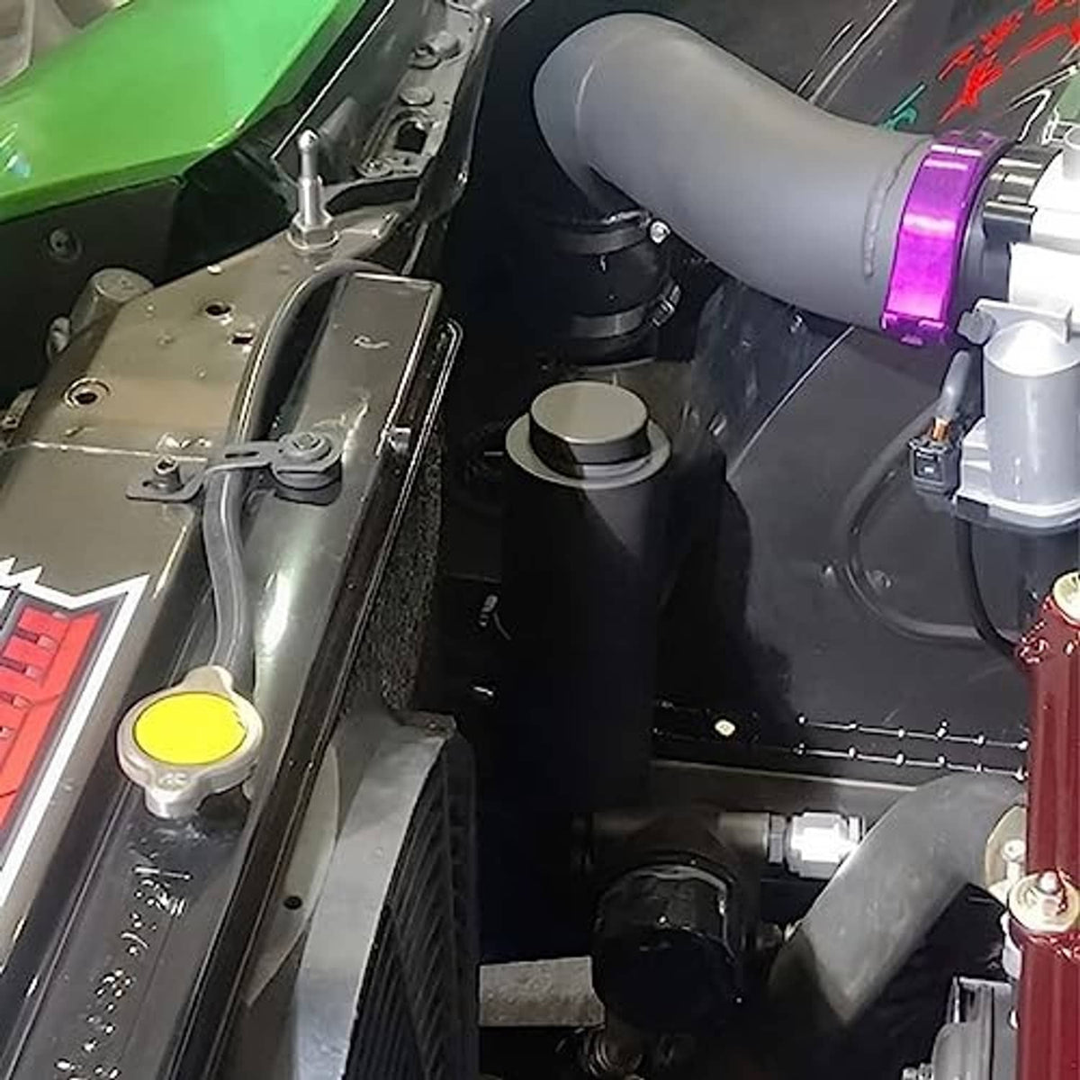 Cylindrical coolant overflow bottle installed in engine bay with connected hoses