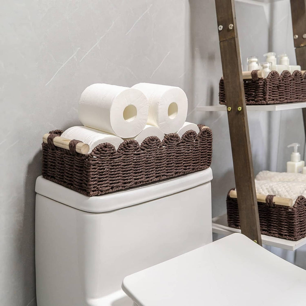 Brown woven toilet paper holder with scalloped top and toilet paper rolls on a tank