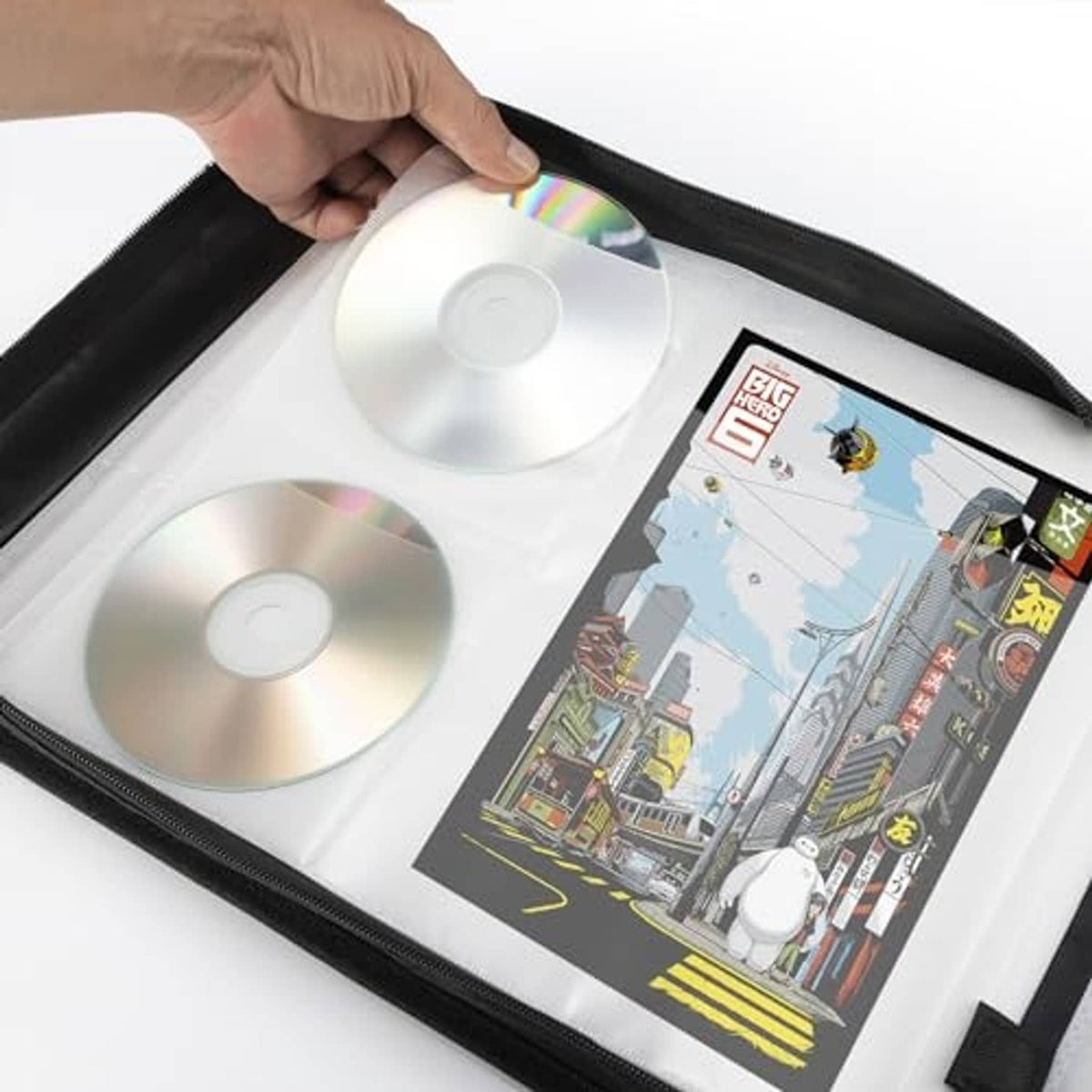 Black DVD case open with discs and a printed booklet; hand lifting the cover