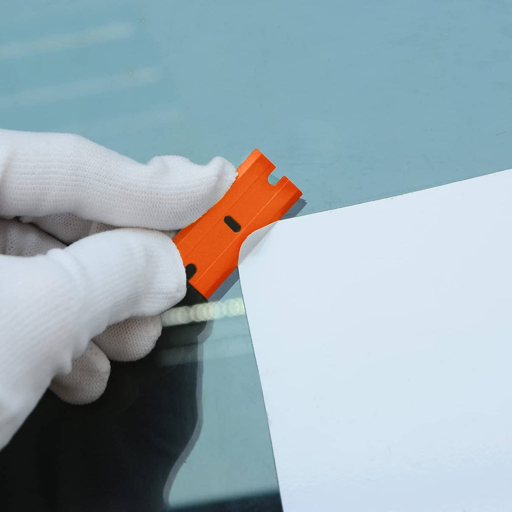 Orange plastic razor blade scraper clipped to a wall edge