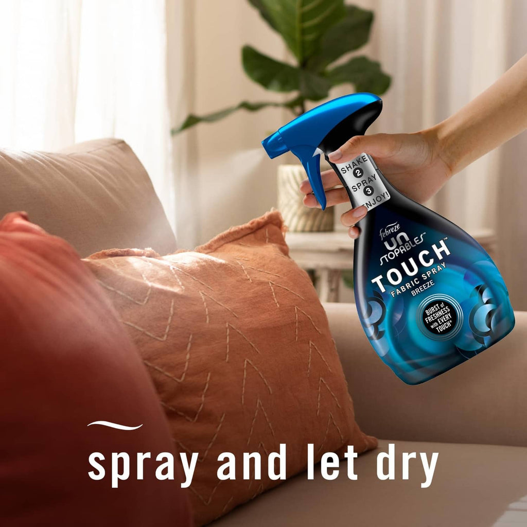 Hand holding blue trigger fabric spray bottle spraying couch cushions