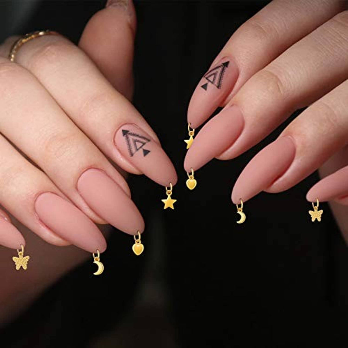 Nail jewelry rings on almond nails featuring gold crescent, star, and heart charms