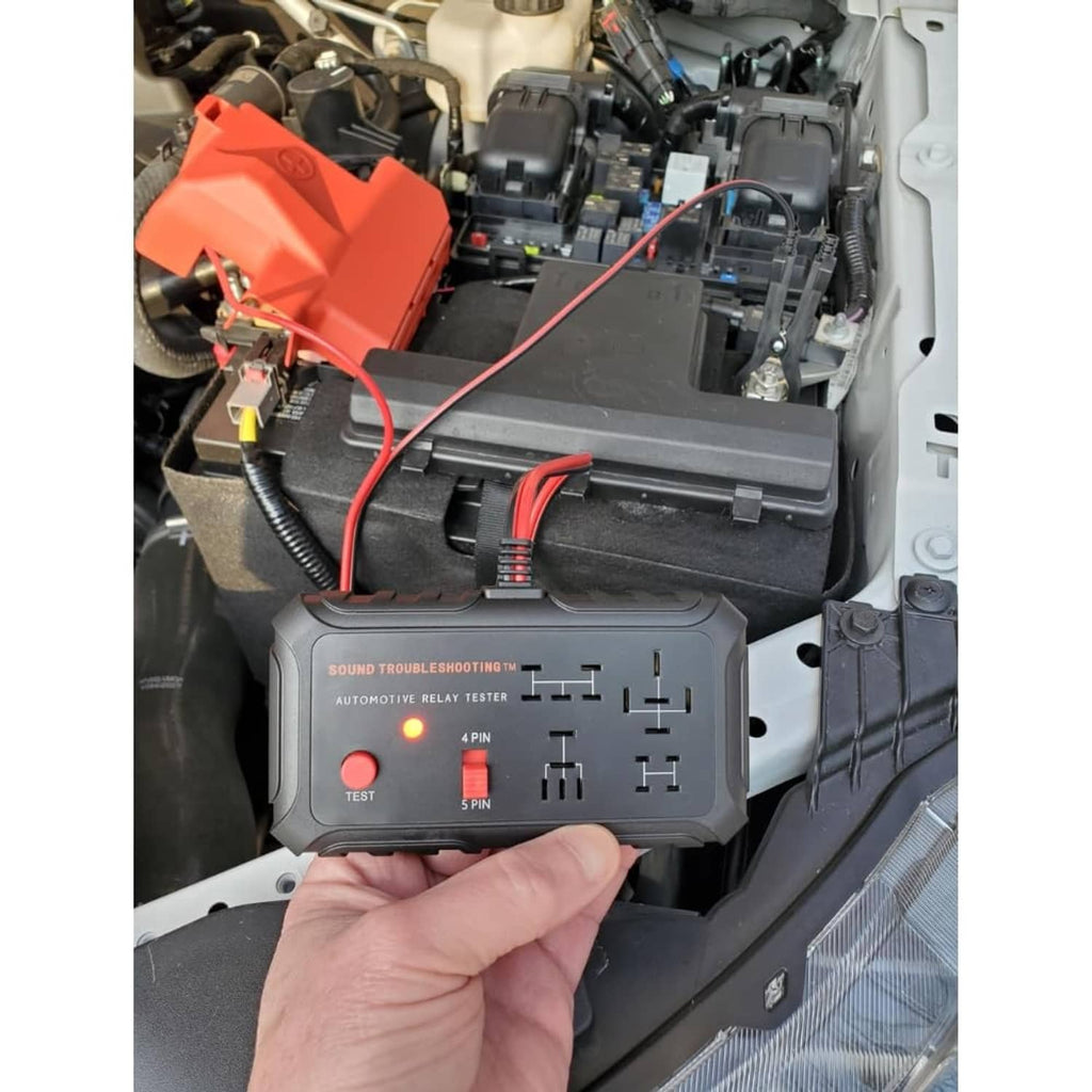 Automotive relay tester connected under the car hood next to red fuse module