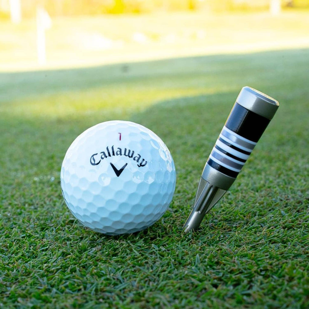 Golf divot tool beside a white Callaway golf ball on green grass