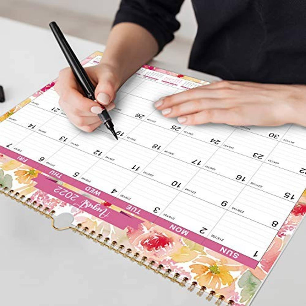 Hand writing dates on a wall calendar with cactus floral print and gold spiral binding