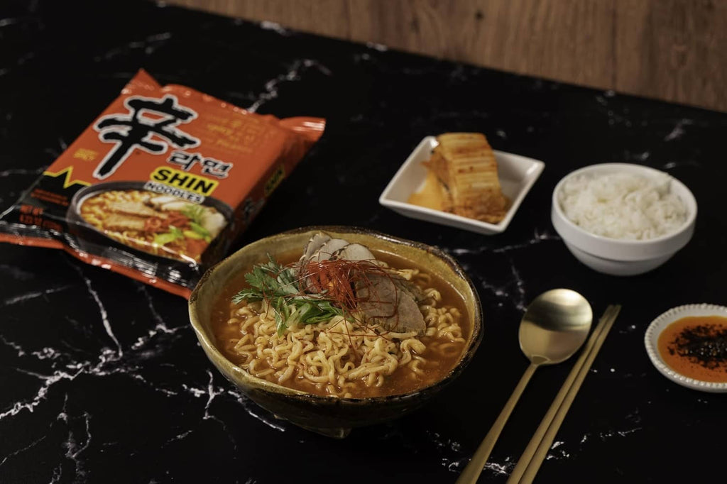 Spicy Korean ramen noodles in a bowl with garnish, with Nongshim Shin packet nearby