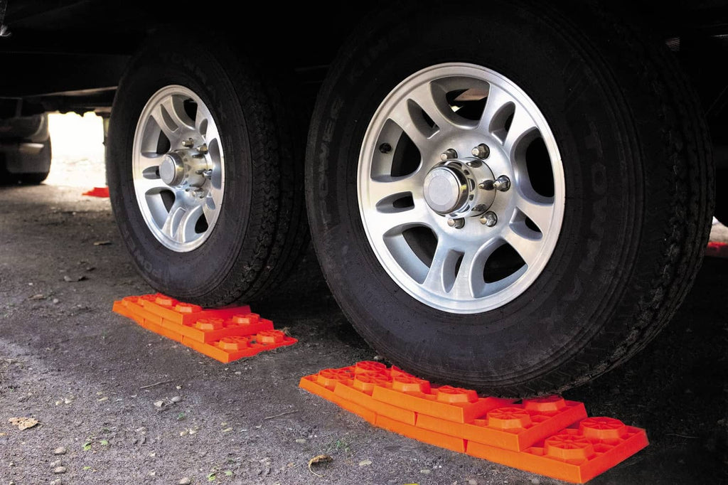 Orange RV leveling blocks under truck tires on asphalt