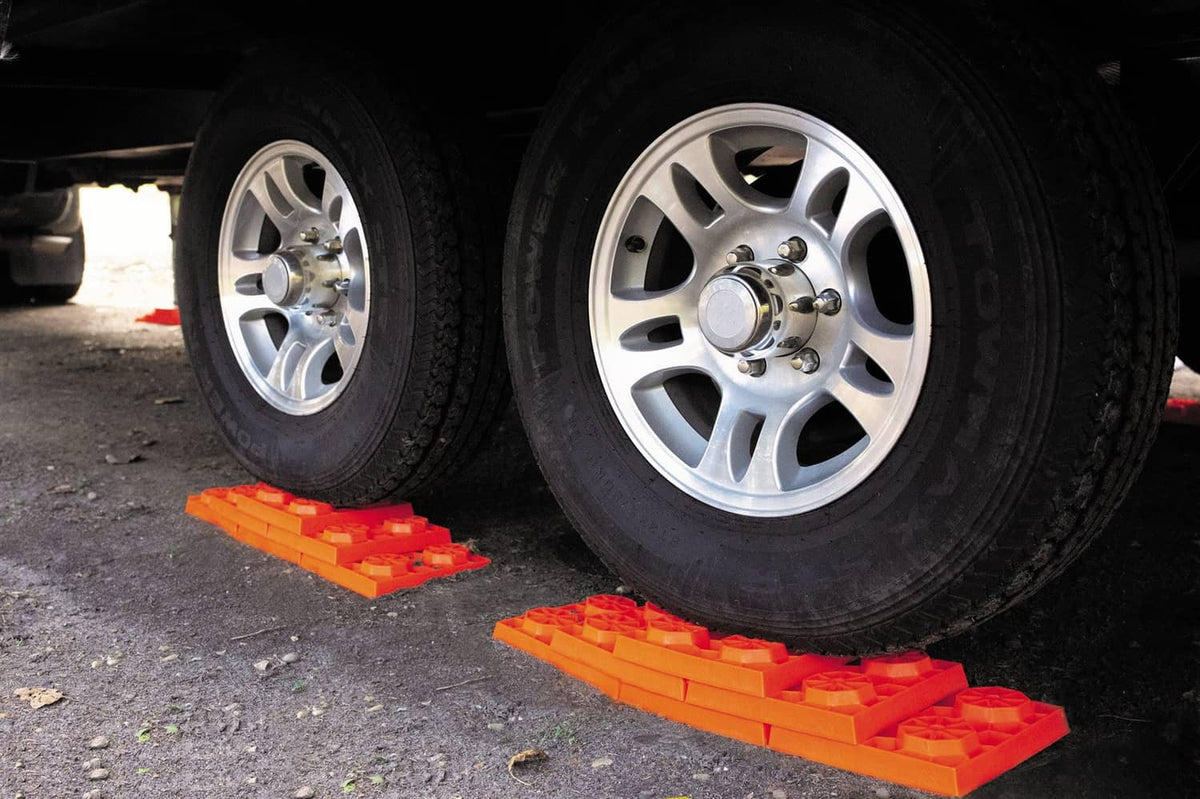 Orange RV leveling blocks under truck tires on asphalt