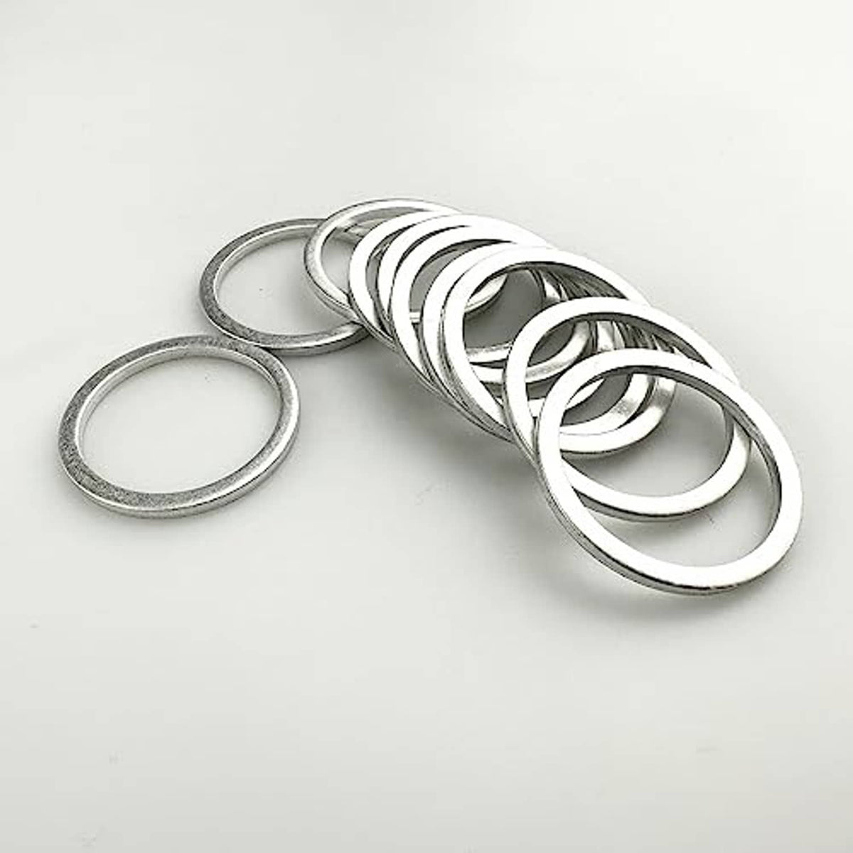 Set of silver aluminum oil drain plug gaskets (washers) stacked and laid on white surface