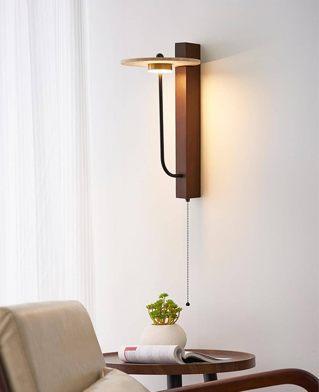 Wall-mounted sconce with round travertine shade, black arm, and dangling pull chain