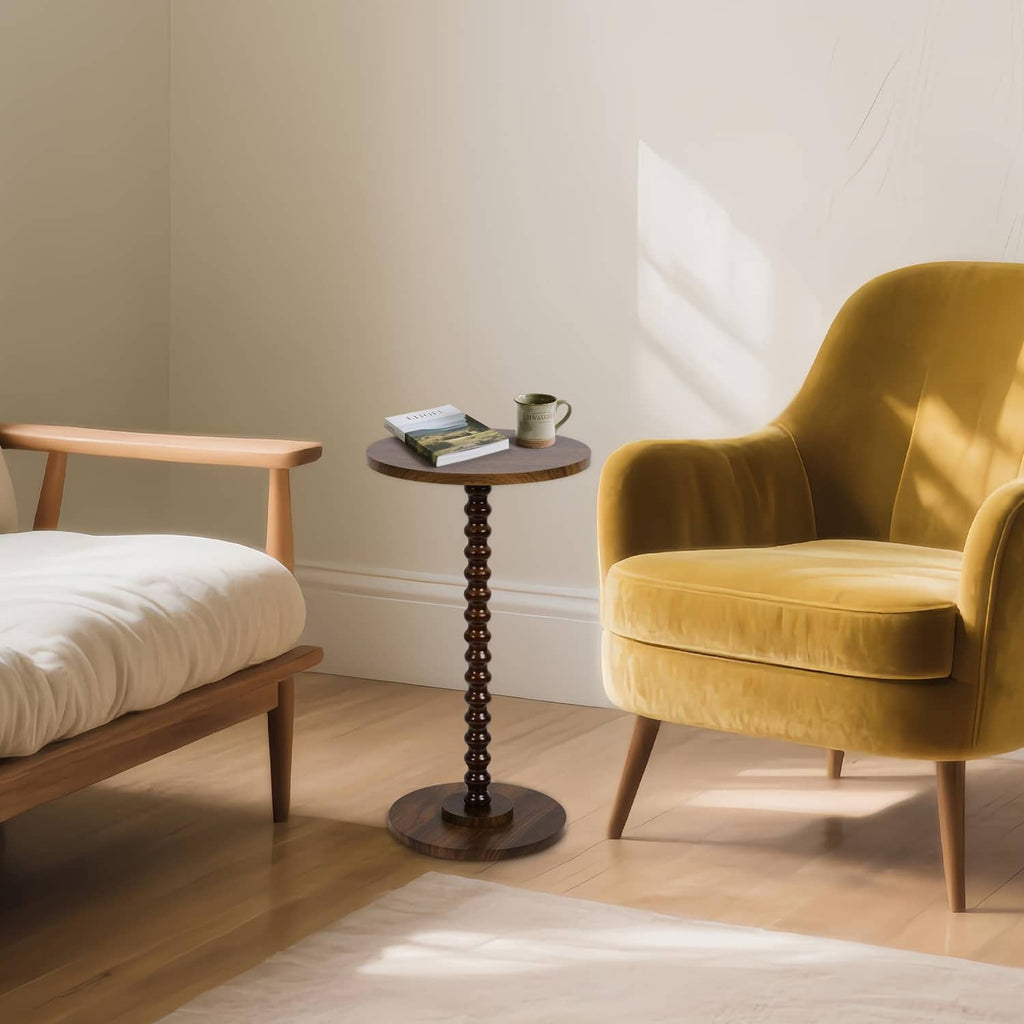 Rustic brown round side table with turned pedestal base next to yellow armchair