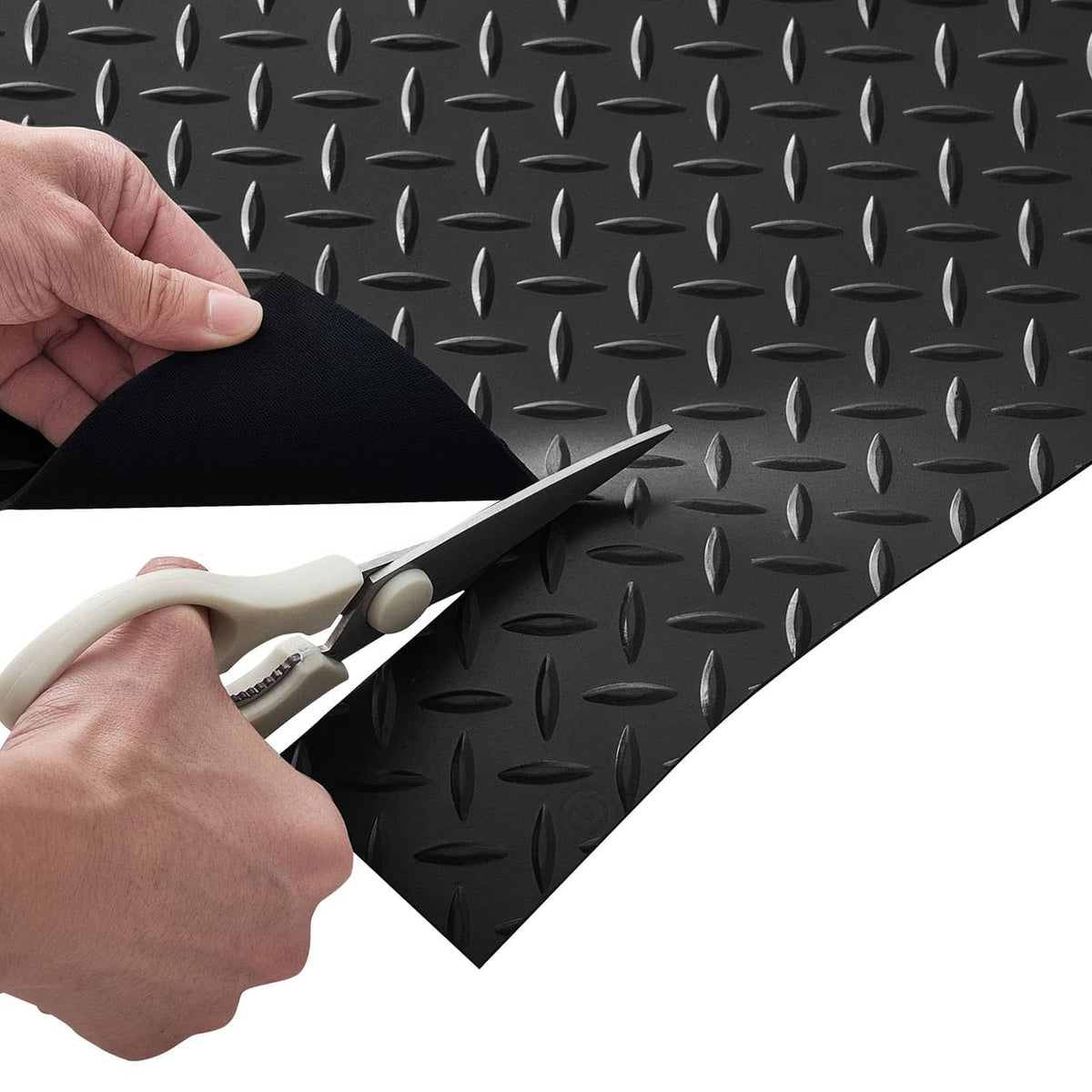 Black rubber garage floor mat being cut to shape with scissors, diamond-textured