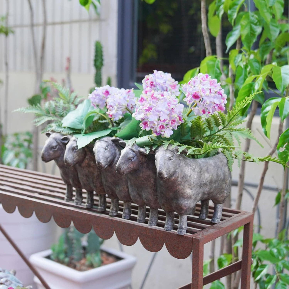 Dark gray resin sheep planter pot holding pink blossoms and greenery
