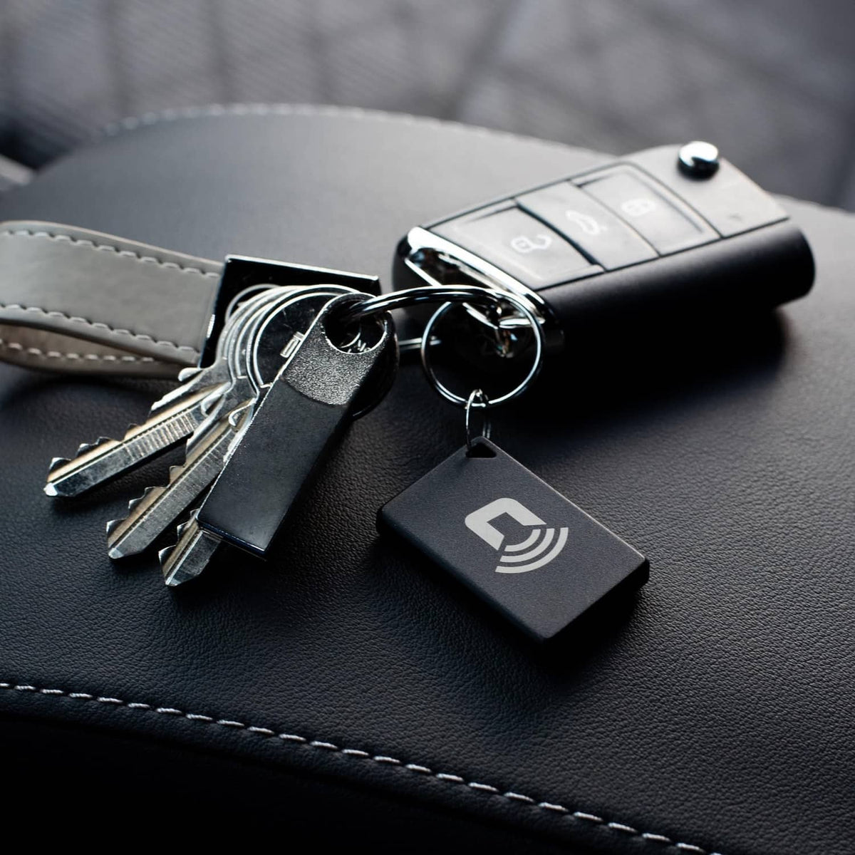 Black CARLOCK Tag 2.0 attached to keyring on leather wallet with spare keys