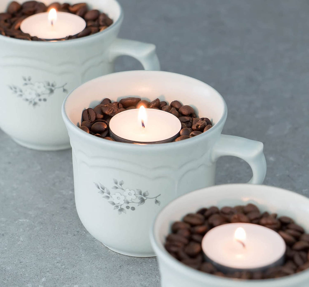 Unscented tea light candles with flames inside white cups filled with dark beads